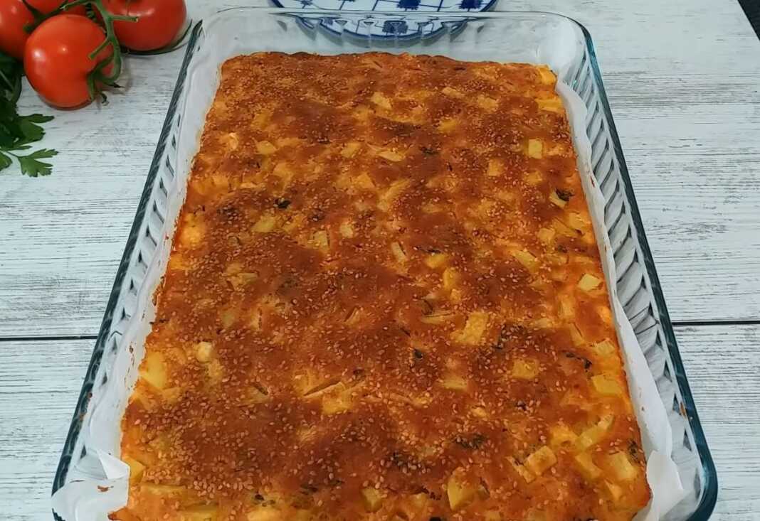 Γρήγορη και οικονομική Πίτα Μια μεγάλη, χρυσαφένια πίτα με φέτα και πατάτες, κομμένη σε τετράγωνα κομμάτια, έτοιμη για σερβίρισμα.