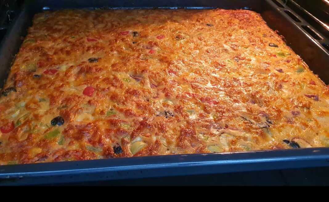 Ένα ταψί πίτας λαχανικών χωρίς φύλλα με τριμμένο τυρί τσένταρ στην επιφάνεια.