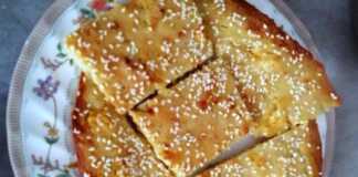 Αφράτη χρυσαφένια τυρόπιτα χωρίς φύλλο, πασπαλισμένη με σουσάμι, κομμένη σε τετράγωνα κομμάτια μέσα στο ταψί.