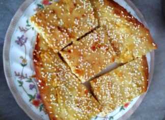 Αφράτη χρυσαφένια τυρόπιτα χωρίς φύλλο, πασπαλισμένη με σουσάμι, κομμένη σε τετράγωνα κομμάτια μέσα στο ταψί.