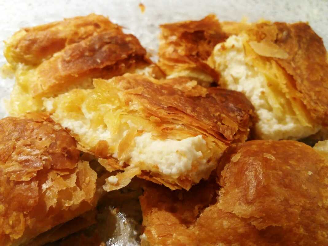 ΜπουγατσοΤυρόπιτα Βελούδινη κρεμένια τυρόπιτα κομμένη σε κομμάτια, με χρυσαφένια, αφράτη σφολιάτα.