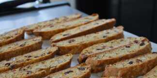 Μακρόστενα τραγανά μπισκότα γεμάτα με κομμάτια αμυγδάλου και αποξηραμένων φρούτων τοποθετημένα πάνω σε αντικολλητικό χαρτί ψησίματος