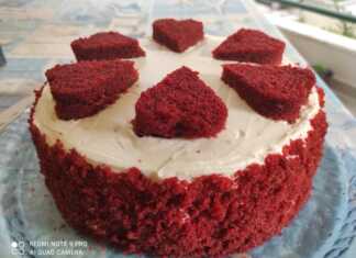 Εντυπωσιακό κόκκινο κέικ Red Velvet με πλούσια λευκή επικάλυψη κρέμας τυριού στολισμένο με κόκκινες καρδιές και θρυμματισμένο παντεσπάνι