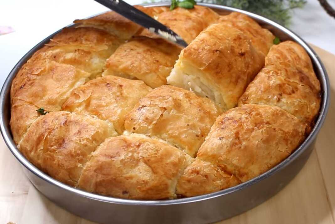 Ένα ροδοκοκκινισμένο τυρόψωμο στο ταψί, κομμένο σε τετράγωνα κομμάτια, με τις στρώσεις της ζύμης και της φέτας να ξεχωρίζουν.