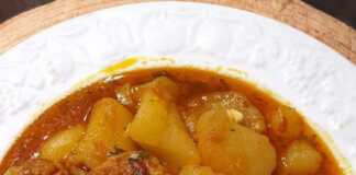 Μια κατσαρόλα με πατάτες κομμένες σε κύβους και τηγανητούς κεφτέδες σε κόκκινη σάλτσα, πασπαλισμένη με μαϊντανό.