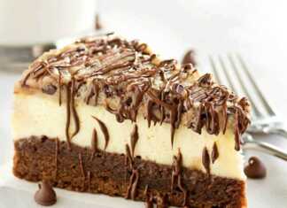 Μια φέτα brownie cheesecake που δείχνει τις τρεις διακριτές στρώσεις: σκούρο brownie στη βάση, λευκό cheesecake στη μέση και μπισκότο στην κορυφή, περιχυμένη με λιωμένη σοκολάτα.