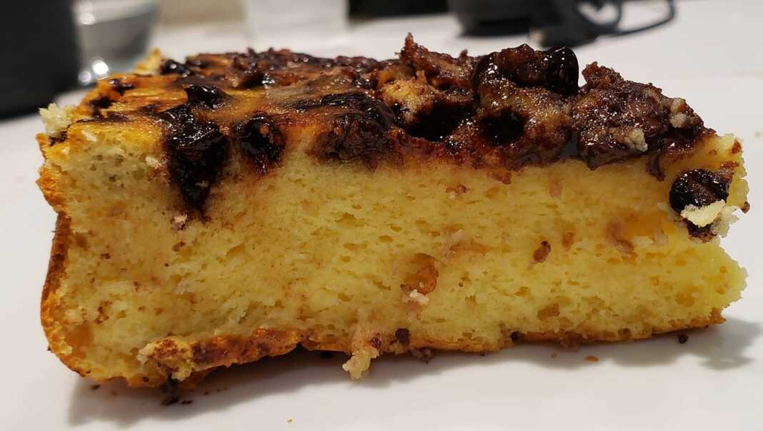 Ένα κομμάτι από ένα πολύ αφράτο, χρυσαφένιο κέικ με λιωμένα chips σοκολάτας στην κορυφή, σερβιρισμένο σε ένα πιάτο.