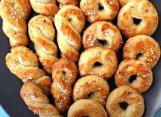 Σειρές από χρυσαφένια κουλουράκια πλεξούδες πασπαλισμένα με σουσάμι πάνω σε αντικολλητικό χαρτί ψησίματος