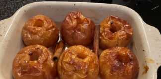 Τέσσερα ψητά μήλα σε ταψί, γεμισμένα με ζάχαρη και περιχυμένα με σάλτσα