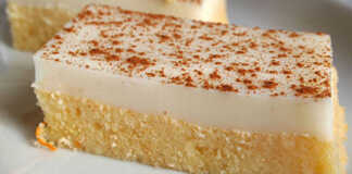 Ένα κομμένο κομμάτι από αφράτο ρεβανί με κίτρινη βάση σιμιγδαλιού και μια λευκή, λεία στρώση κρέμας στην κορυφή, πασπαλισμένο με κανέλα.