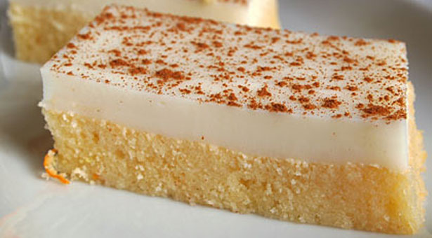 revaniMalembi Ένα κομμένο κομμάτι από αφράτο ρεβανί με κίτρινη βάση σιμιγδαλιού και μια λευκή, λεία στρώση κρέμας στην κορυφή, πασπαλισμένο με κανέλα.