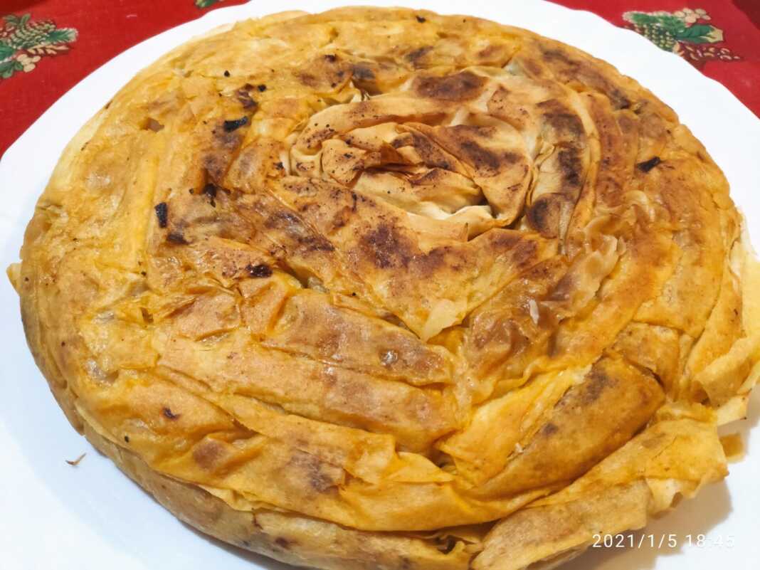 Μια χρυσαφένια, στρογγυλή πίτα με φύλλο κρούστας, ψημένη σε τηγάνι, κομμένη σε κομμάτια, με τη γέμιση από λάχανο τουρσί να διακρίνεται.