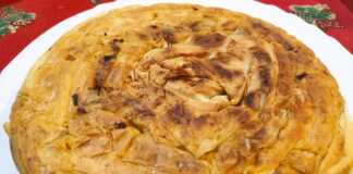 Μια χρυσαφένια, στρογγυλή πίτα με φύλλο κρούστας, ψημένη σε τηγάνι, κομμένη σε κομμάτια, με τη γέμιση από λάχανο τουρσί να διακρίνεται.