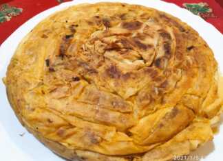 Μια χρυσαφένια, στρογγυλή πίτα με φύλλο κρούστας, ψημένη σε τηγάνι, κομμένη σε κομμάτια, με τη γέμιση από λάχανο τουρσί να διακρίνεται.