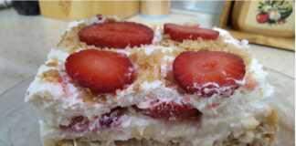 Ένα κομμάτι μιλφέιγ με στρώσεις χρυσής σφολιάτας, λευκής κρέμας και φρέσκων κόκκινων φραουλών, πασπαλισμένο με άχνη ζάχαρη, σε ένα λευκό πιάτο.