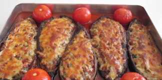 Ένα ταψί με γεμιστές μελιτζάνες σε σχήμα βαρκούλας, γεμισμένες με κιμά και καλυμμένες με λιωμένο τυρί, ανάμεσα σε μικρές ντομάτες και κομμάτια πιπεριάς.