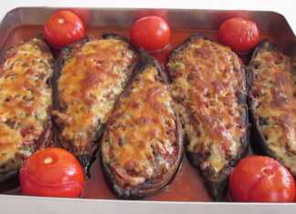 Ένα ταψί με γεμιστές μελιτζάνες σε σχήμα βαρκούλας, γεμισμένες με κιμά και καλυμμένες με λιωμένο τυρί, ανάμεσα σε μικρές ντομάτες και κομμάτια πιπεριάς.