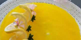 Ένα ολόκληρο cheesecake λεμονιού σε ένα στρογγυλό σκεύος, με λαμπερή κίτρινη επίστρωση ζελέ και φέτες φρέσκου λεμονιού για διακόσμηση