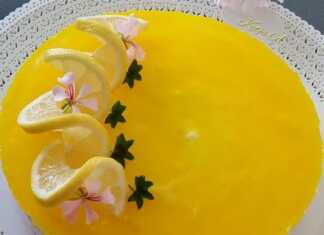 Ένα ολόκληρο cheesecake λεμονιού σε ένα στρογγυλό σκεύος, με λαμπερή κίτρινη επίστρωση ζελέ και φέτες φρέσκου λεμονιού για διακόσμηση