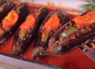 Ένα πυρέξ γεμάτο μελιτζάνες κομμένες στη μέση και γεμιστές με κιμά, ντομάτα και πιπεριά, έτοιμες για ψήσιμο ή ψημένες.