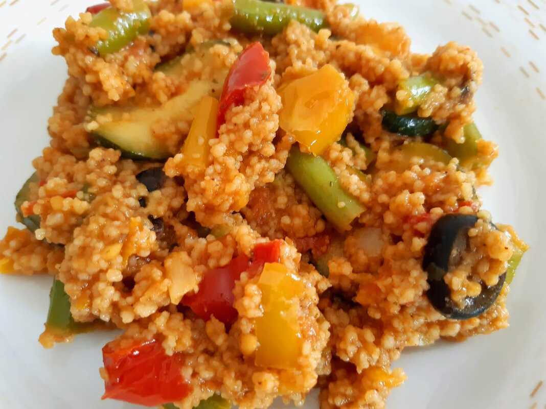 kuskus Πιάτο με πολύχρωμο κους-κους αναμεμειγμένο με διάφορα ψιλοκομμένα λαχανικά, όπως πιπεριές, κολοκυθάκια και καρότα.