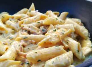 Ένα πιάτο με πέννες καλυμμένες με πλούσια κίτρινη σάλτσα κάρι κομμάτια κοτόπουλου μπέικον και λιωμένο τυρί τσένταρ πασπαλισμένες με μαϊντανό