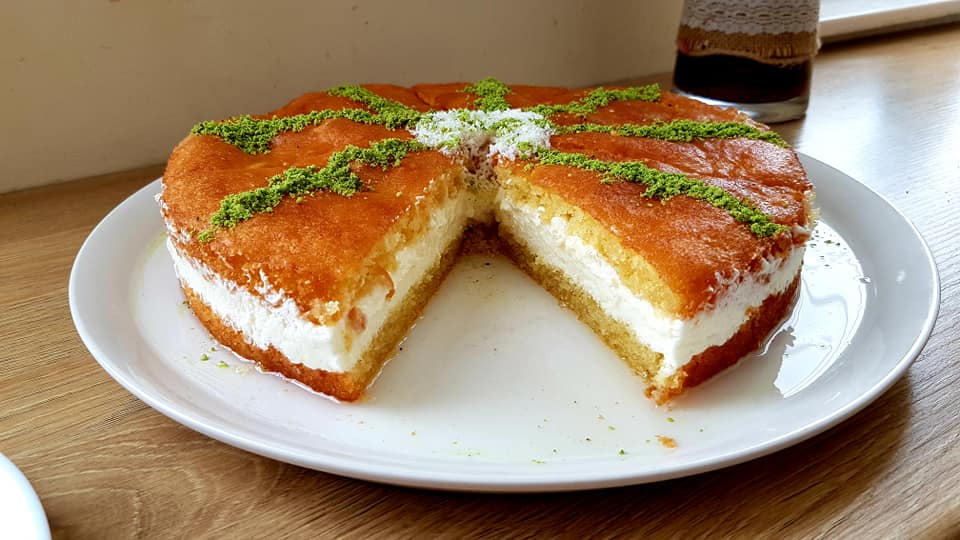 babas Μία ολόκληρη Τούρτα Μπαμπάς σε πιατέλα, διακοσμημένη με φιστίκι Αιγίνης και καρύδα