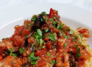 Πιάτο με μακαρόνια, κομμάτια μπακαλιάρου, κόκκινη σάλτσα ντομάτας, ελιές και μαϊντανό, έτοιμο για σερβίρισμα.