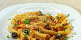 Ένα πιάτο με πένες ανακατεμένες με κόκκινη σάλτσα ντομάτας, πράσινο βασιλικό και μαύρες ελιές.