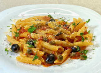 Ένα πιάτο με πένες ανακατεμένες με κόκκινη σάλτσα ντομάτας, πράσινο βασιλικό και μαύρες ελιές.