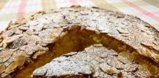 Κοντινό πλάνο σε μία φέτα από Κέικ Πορτοκάλι Καρότο Αμύγδαλο, που αναδεικνύει την υφή και τα ψιλοκομμένα καρότα και αμύγδαλα.