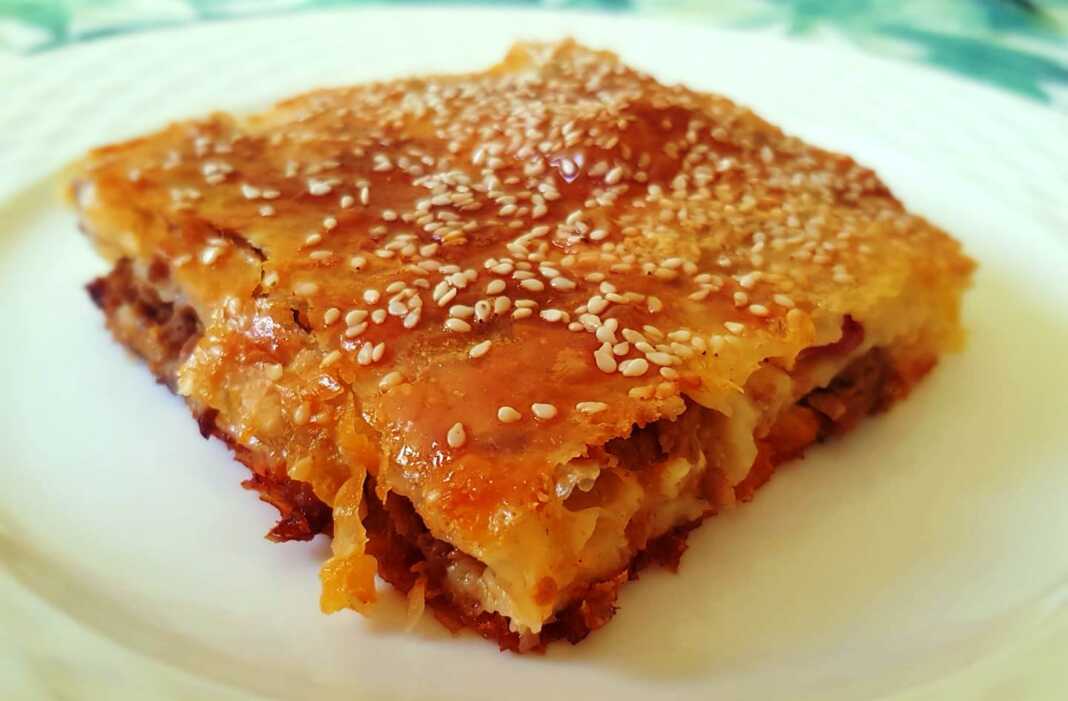 kimadopita Ένα ταψί με κομμένη κιμαδόπιτα, με χρυσαφένια κρούστα και σουσάμι.