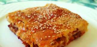 Ένα ταψί με κομμένη κιμαδόπιτα, με χρυσαφένια κρούστα και σουσάμι.