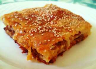 Ένα ταψί με κομμένη κιμαδόπιτα, με χρυσαφένια κρούστα και σουσάμι.