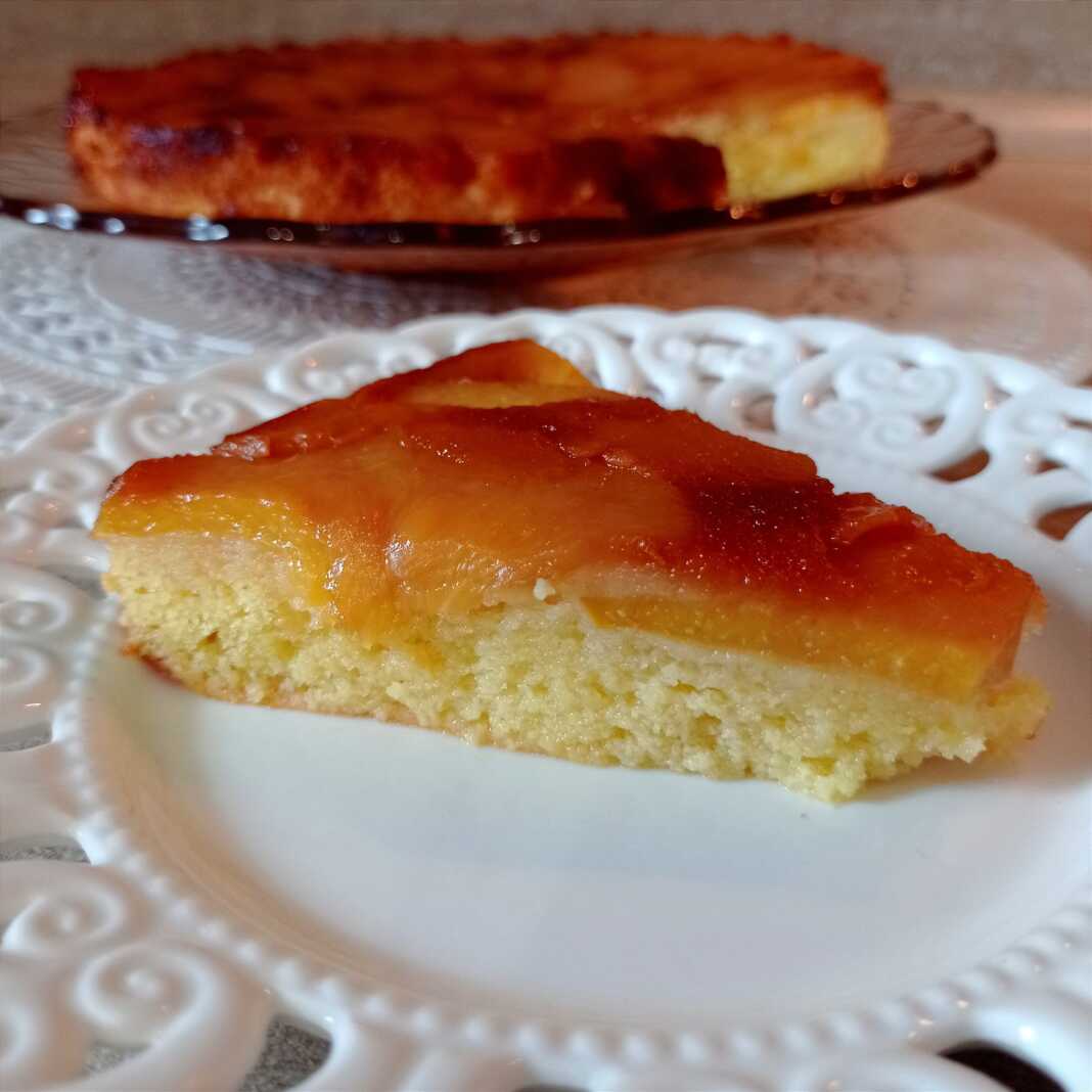 Ένα κομμάτι από ανάποδο κέικ με καραμελωμένα ροδάκινα στην κορυφή, τοποθετημένο σε ένα πιάτο.