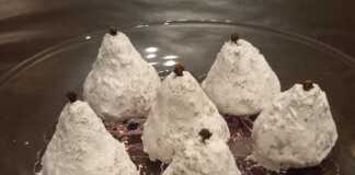 Λευκά Παραδοσιακά Αμυγδαλωτά Μυτιλήνης σε σχήμα αχλαδιού, πασπαλισμένα με ζάχαρη άχνη, με ένα γαρύφαλλο στην κορυφή.