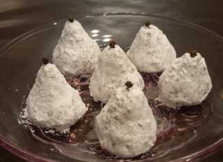 Λευκά Παραδοσιακά Αμυγδαλωτά Μυτιλήνης σε σχήμα αχλαδιού, πασπαλισμένα με ζάχαρη άχνη, με ένα γαρύφαλλο στην κορυφή.