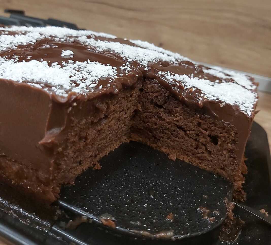 Ένα κομμάτι λαχταριστού κέικ σοκολάτας, περιχυμένο με γυαλιστερό γλάσο κακάο και πασπαλισμένο με τριμμένη καρύδα.