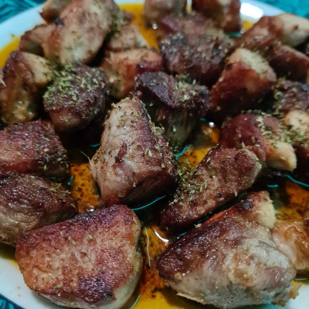 Καλοτηγανισμένα κομμάτια χοιρινού λαιμού μέσα στο τηγάνι με καραμελωμένα κρεμμύδια και φρέσκια ρίγανη