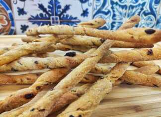 Μακρόστενα τραγανά κριτσίνια σιμιγδαλιού με ορατά κομμάτια λιαστής ντομάτας και ελιάς αραδιασμένα σε ταψί με αντικολλητικό χαρτί