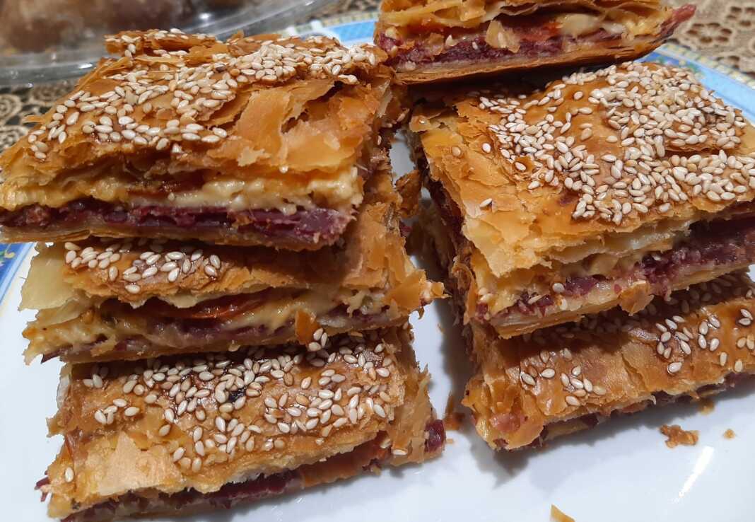 Κομμάτια Παστουρμαδόπιτα, φρεσκοψημένη, με χρυσαφένια κρούστα και σουσάμι στην επιφάνεια.