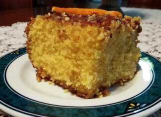 Κομμάτι πορτοκαλόπιτας σε πιατέλα, με πλούσιο χρυσαφένιο σιρόπι, πασπαλισμένο με χοντροκομμένα αμύγδαλα, δείχνοντας την αφράτη υφή της.