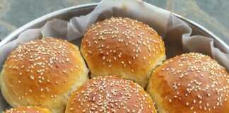 Ένα ολόκληρο, χρυσαφένιο, στρογγυλό ψωμί σε σχήμα μαργαρίτας, πασπαλισμένο με σουσάμι, πάνω σε ξύλινη επιφάνεια.