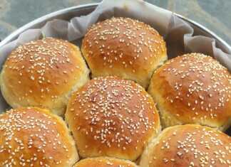 Ένα ολόκληρο, χρυσαφένιο, στρογγυλό ψωμί σε σχήμα μαργαρίτας, πασπαλισμένο με σουσάμι, πάνω σε ξύλινη επιφάνεια.