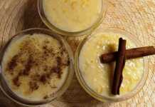 Μπολ γεμάτα με λευκό, κρεμώδες ρυζόγαλο, με πορτοκαλί ξύσμα και πιθανώς κομματάκια φρούτου στην επιφάνεια.