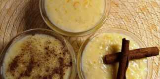 Μπολ γεμάτα με λευκό, κρεμώδες ρυζόγαλο, με πορτοκαλί ξύσμα και πιθανώς κομματάκια φρούτου στην επιφάνεια.