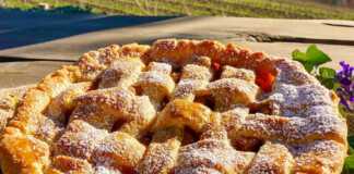 Μια ολόκληρη, χρυσαφένια μηλόπιτα με πλέγμα στην κορυφή, πασπαλισμένη με άχνη ζάχαρη, πάνω σε ένα ξύλινο τραπέζι.