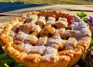 Μια ολόκληρη, χρυσαφένια μηλόπιτα με πλέγμα στην κορυφή, πασπαλισμένη με άχνη ζάχαρη, πάνω σε ένα ξύλινο τραπέζι.