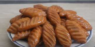 Ένα πιάτο με χρυσαφένια, μακρόστενα φοινίκια γλυκά, γυαλιστερά από το μέλι, με σχέδια στην επιφάνειά τους.