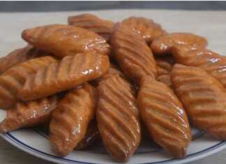 Ένα πιάτο με χρυσαφένια, μακρόστενα φοινίκια γλυκά, γυαλιστερά από το μέλι, με σχέδια στην επιφάνειά τους.